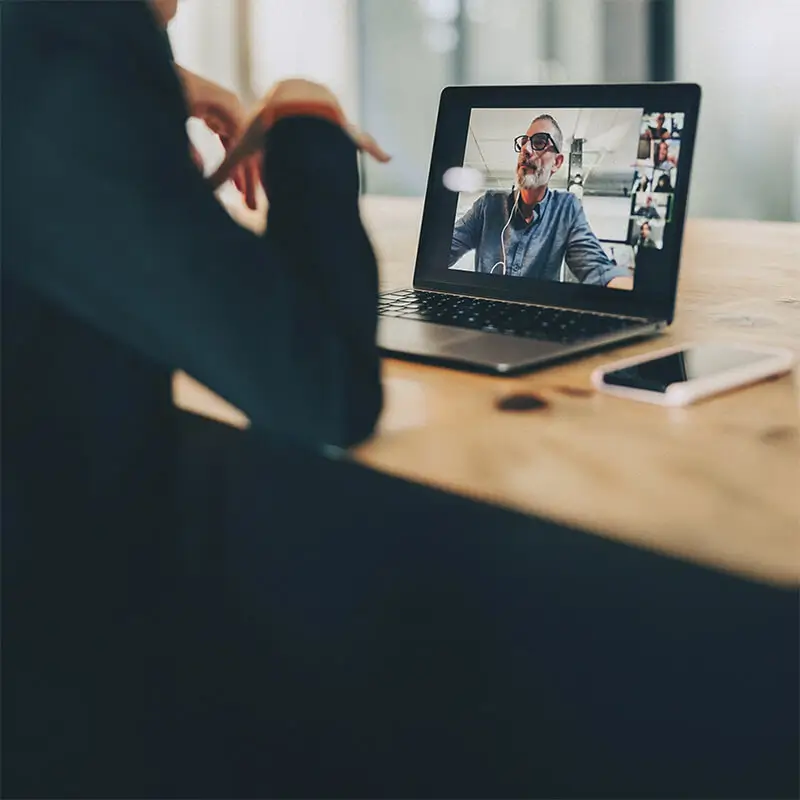 Reunión virtual a través de una videollamada en un portátil. Un profesional se comunica en un entorno de trabajo híbrido, resaltando el teletrabajo, la digitalización y la conectividad global.