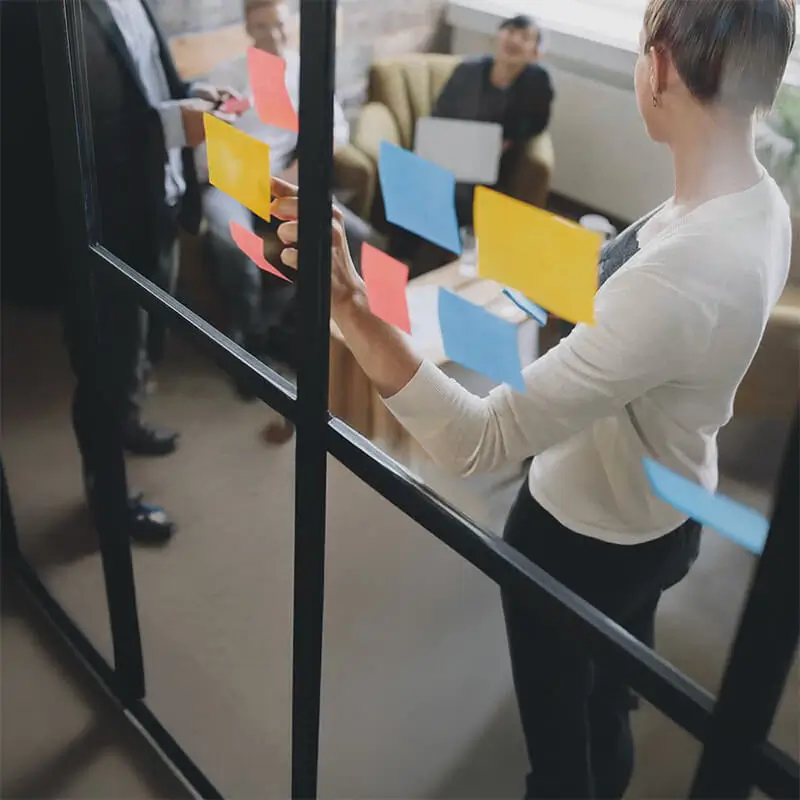 Colaboración en equipo con notas adhesivas en una pared de vidrio. Un equipo de trabajo creativo planifica estrategias en una oficina moderna. Conceptos clave: brainstorming, innovación y productividad.